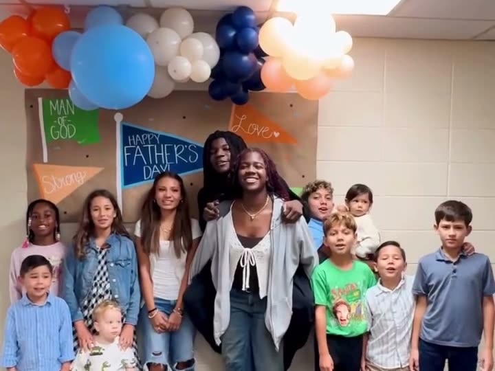 A group of smiling kids and teens standing in front of balloons and a Father's Day banner